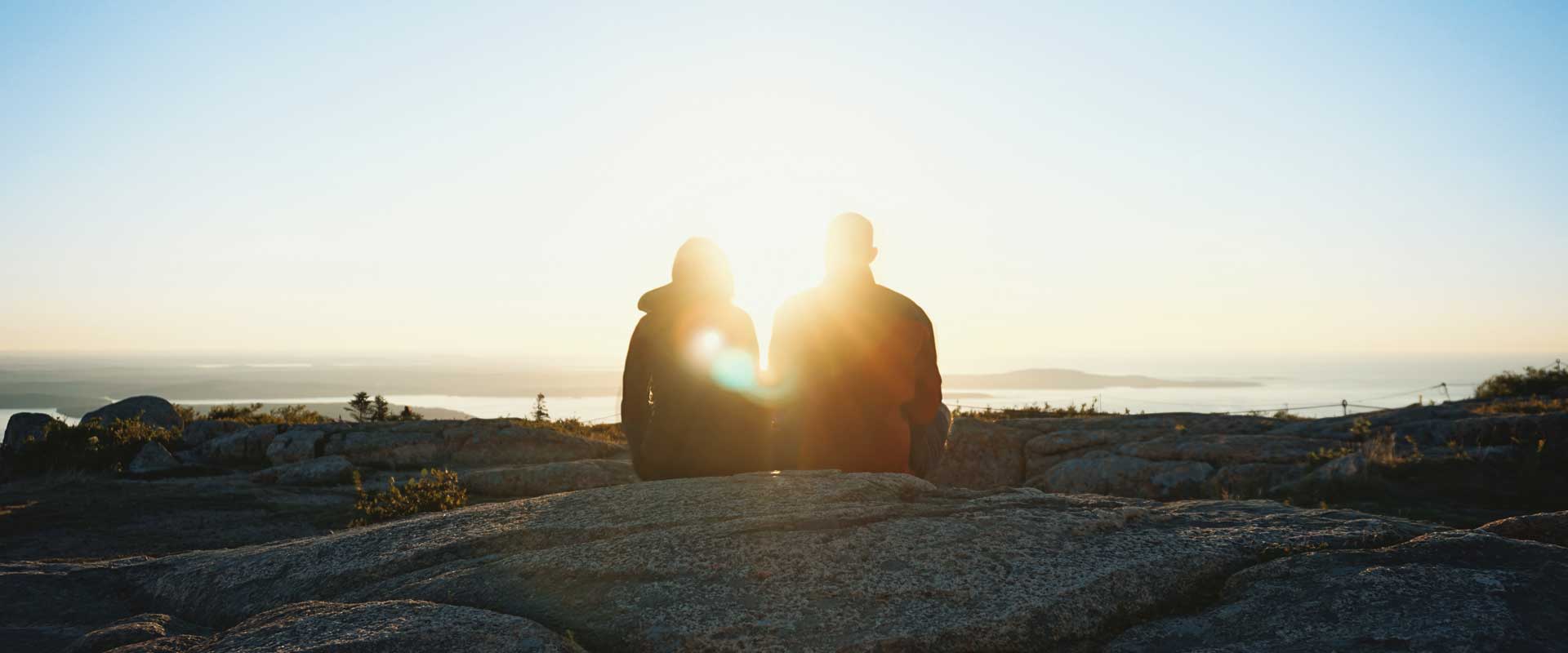 A couple sit side-by-side while enjoying a scenic landscape near the coast