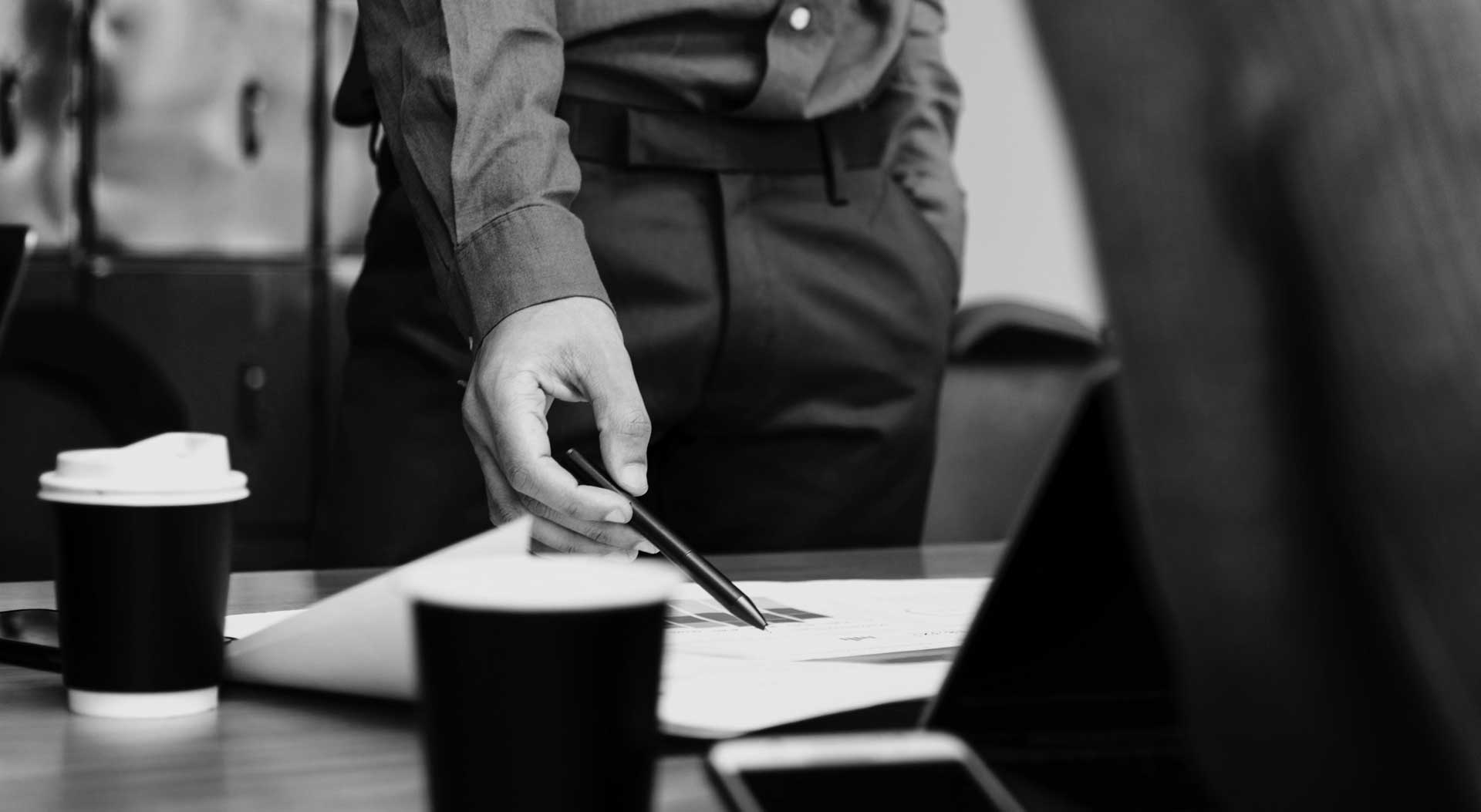 Man wearing business attire reviews a document with a black pen while standing at a desk