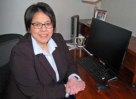 woman with black hair wearing glasses and suit at desk in front of computer